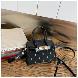 Detail of a mini black polka dot handbag with gold twist lock on a wooden surface