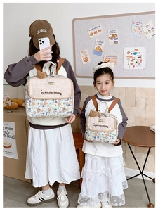 Detail of floral and checkered parent-child backpacks with plush bear charms in a bakery setting