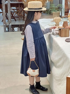 Detail of a girl wearing a navy blue pinafore dress and checkered shirt in a cozy room