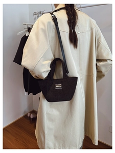 Détail du sac seau en velours côtelé noir avec logo sur un trench-coat beige