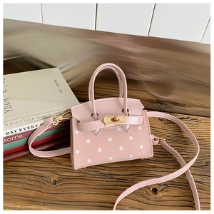 Detailed close-up of pink polka dot mini crossbody bag with golden turn-lock on wood