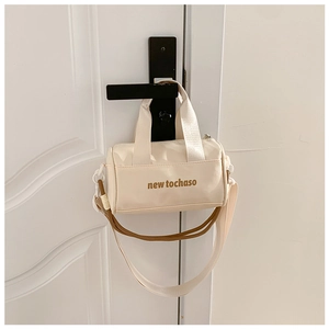 Detail of a creamy white cylindrical bucket bag with a brown strap hanging on a door handle