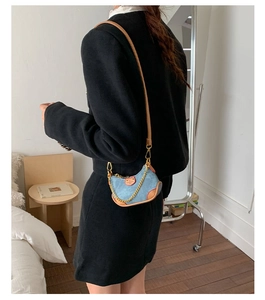 Détail du mini sac demi-lune en denim bleu avec bordures en cuir brun et chaîne dorée