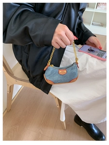 Detail of mini denim handbag with leather trim and gold chain strap held by model