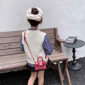Red polka dot mini child crossbody bag with top handle and gold hardware in outdoor setting