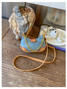 Détail du sac croissant en denim bleu avec garniture en cuir brun et chaîne dorée