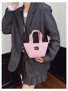 Détail d'un sac seau en velours rose avec écusson en cuir porté par un mannequin sur un blazer