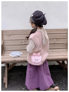 Close-up of pink plaid kids crossbody bag with 3D bow and lace trim on a wooden bench