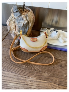 Détail du mini sac dumpling en cuir crème avec chaîne dorée et bords rouges contrastés