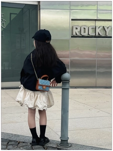 Outdoor street view of a child wearing a blue quilted denim mini crossbody chain bag