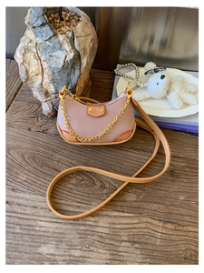Détail d'un mini sac hobo rose avec chaîne dorée sur une table en bois décorée