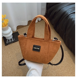 Détail du sac seau en velours côtelé marron avec écusson en cuir et bandoulière