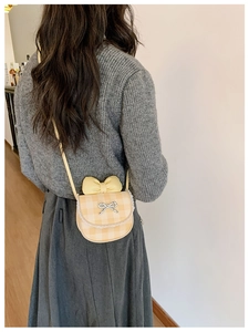 Detail of mini plaid crossbody bag with lace trim and bow charm worn by a child