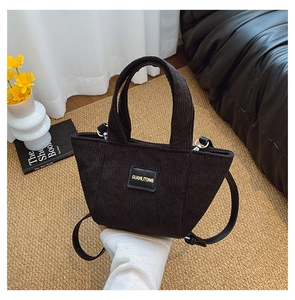Détail du sac seau en velours côtelé noir avec écusson en cuir et bandoulière réglable