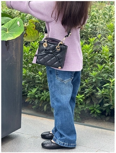 Detail of children's black quilted crossbody bag with bow decoration and matching shoes