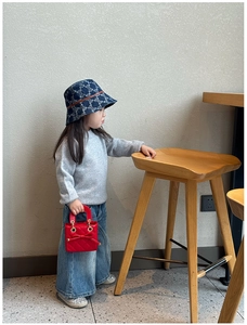 Close-up of a red quilted mini handbag with a bow and gold chain on a child model