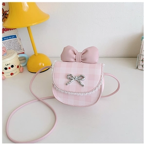 Detailed view of pink plaid kids crossbody bag with leather bow and lace trim on white desk