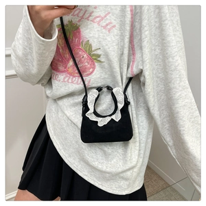 Détail d'un mini sac bandoulière en daim noir avec dentelle blanche et fine sangle réglable