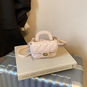 Detail of pink quilted mini bag with gold twist lock and shoulder strap on a book