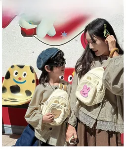 Détail du sac bandoulière en toile beige avec écussons de dessin animé et sangle réglable