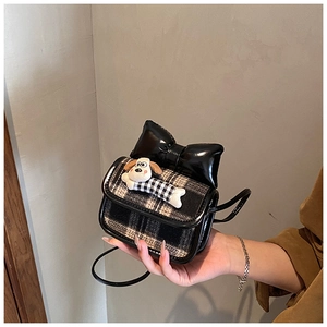 Close-up of mini plaid crossbody bag with black bow and cute cartoon dog plush accessory