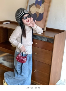 Child wearing beige knit sweater and denim jeans with a red polka dot bow handbag