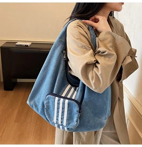 Detailed view of blue denim tote bag featuring white triple stripes and large side pockets