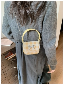 Detail of mini plaid handbag with yellow leather handle, lace trim and silver metal bow