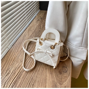 Detail of white quilted mini handbag featuring a delicate bow and gold hardware