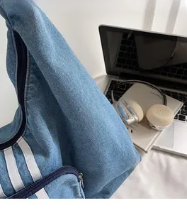 Detail of blue denim tote bag with triple white stripes and laptop on office desk