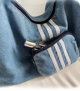 Detail of blue denim tote bag featuring a front zipper pocket and white stripe accents