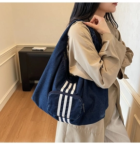Detail of blue denim tote bag with three white stripes and functional front zipper pocket