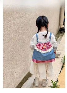 Detail display of a blue denim and red plaid drawstring backpack for kids with lace trim