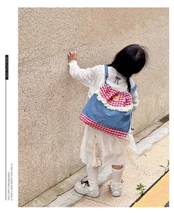 Detailed view of child wearing blue denim drawstring backpack with red gingham and lace