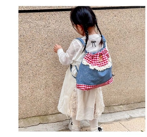 Detail of child wearing blue denim backpack with red plaid and white lace trim
