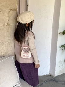 Detail of child wearing a creamy white bow crossbody bag with pink lace handle