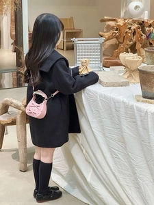 Rear view of a girl wearing a pink bow crossbody bag with a black wool coat