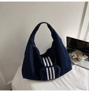 Detail view of deep blue denim hobo bag featuring three white sporty stripes and laptop