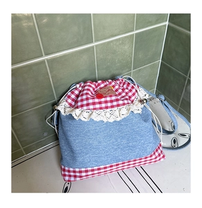Close-up of denim drawstring bag featuring lace trim and red gingham accents