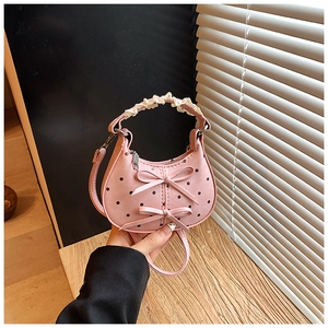 Detail of pink polka dot handbag with bow accents and lace handle held by hand