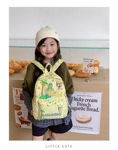 Toddler backpack with monkey banana print worn by a girl in a cozy bakery setting