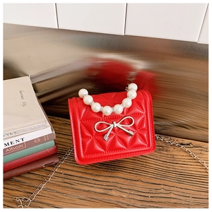 Détail d'un mini sac matelassé rouge avec poignée en perles et nœud argenté élégant