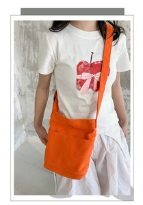 Detail of orange washed canvas crossbody bag with front pocket shown on a model