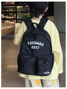 Detail view of large capacity black backpack with white TOCHASO lettering and dual zip pockets