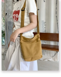 Detail of ginger yellow canvas crossbody bag featuring front pockets and adjustable strap