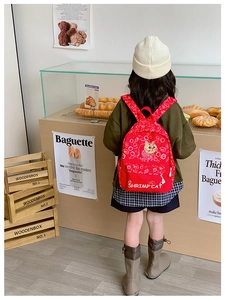 Rear view of a red cartoon cat canvas backpack for kids shown in a lifestyle bakery setting