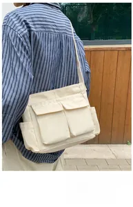 Detail of a cream canvas messenger bag with double front flap pockets on a model