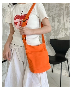 Detail of orange canvas crossbody bag featuring an adjustable strap and external pocket