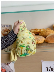 Gelbe Kinder-Brusttasche mit grünem Affen-Druck im Detail vor einer Bäckerei-Szene
