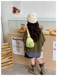 Detail der gelben Kinder-Brusttasche mit Affen-Print, getragen von einem Kind in Bäckerei